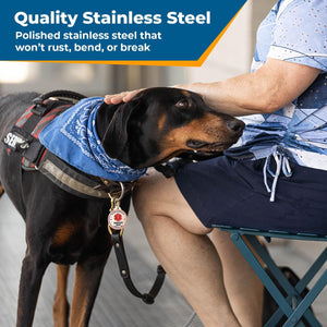 Service dog wearing a stainless steel ID tag beside a seated handler; Quality Stainless Steel, will not rust, bend, or break