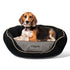 Front view of round black embroidered waterproof dog bed with raised bolsters and removable cushion, small dog seated for scale