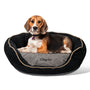 Front view of round black embroidered waterproof dog bed with raised bolsters and removable cushion, small dog seated for scale