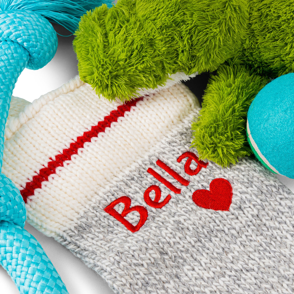 Close-up of light gray knit Christmas stocking showcasing red embroidered name Bella and red heart on white background