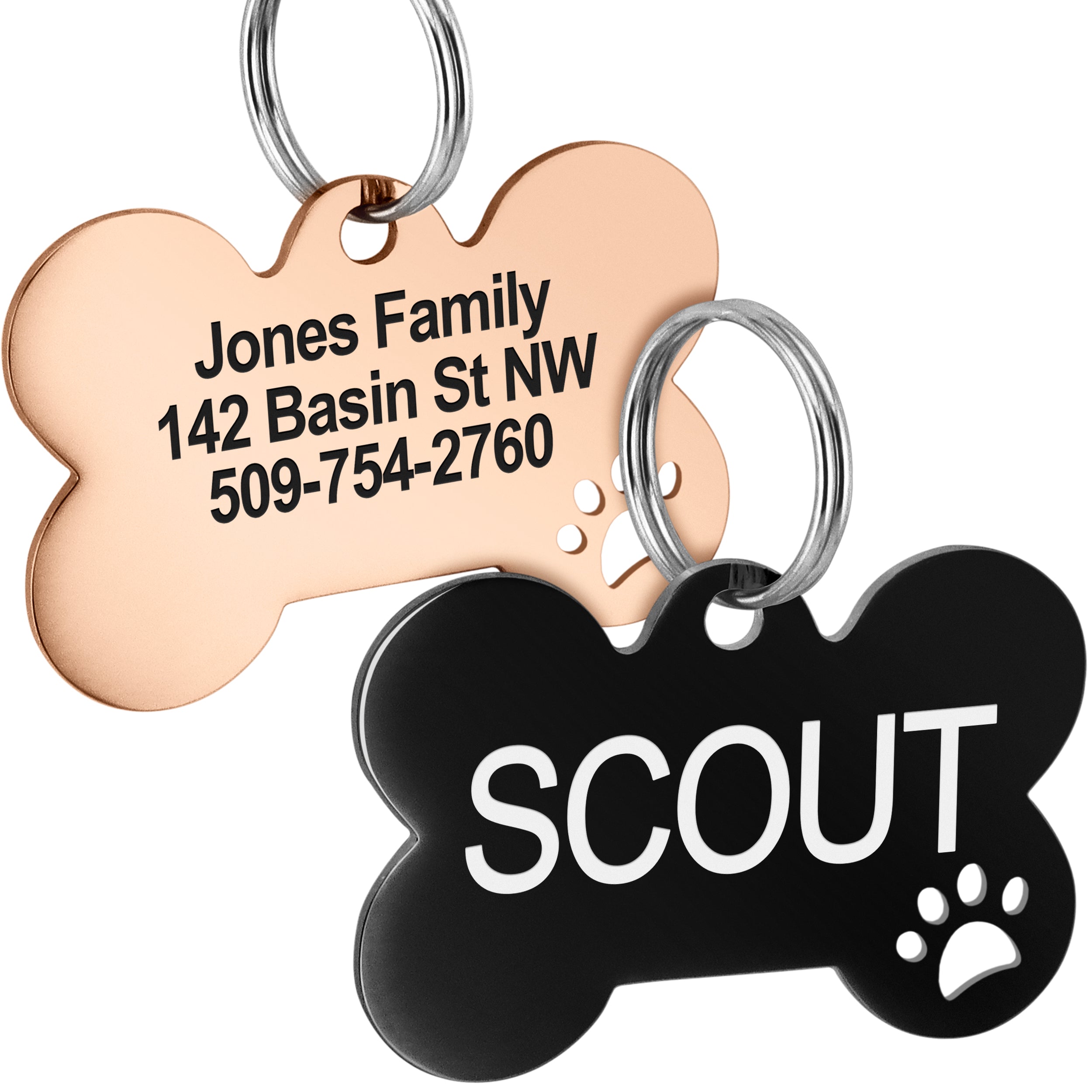 Close-up front view of bone-shaped dog ID tags (rose gold and black) showing paw cutout, sample engraved address and rings on white background