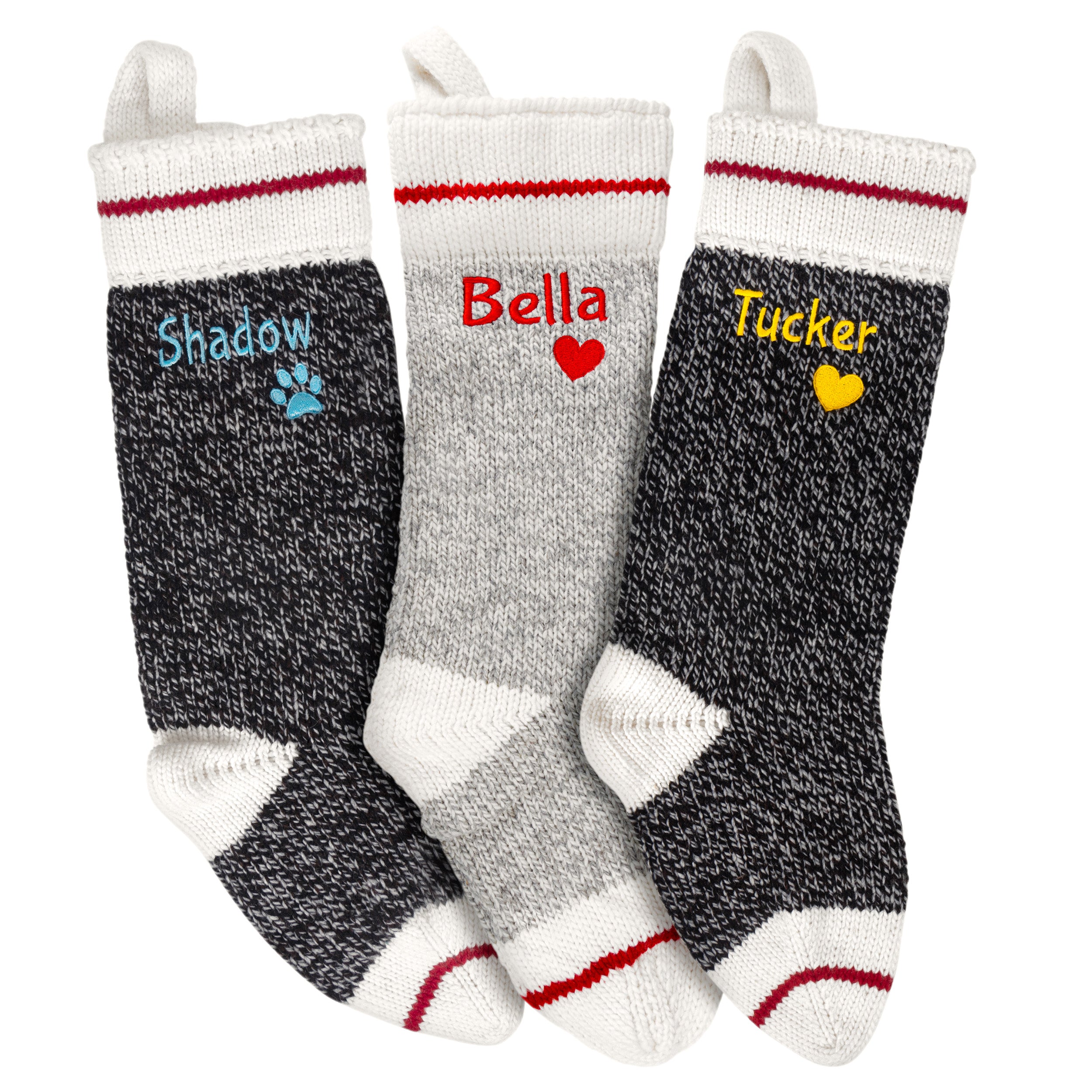 Front view of three hand-knit wool personalized Christmas stockings showing embroidered names and heart or paw motifs on white