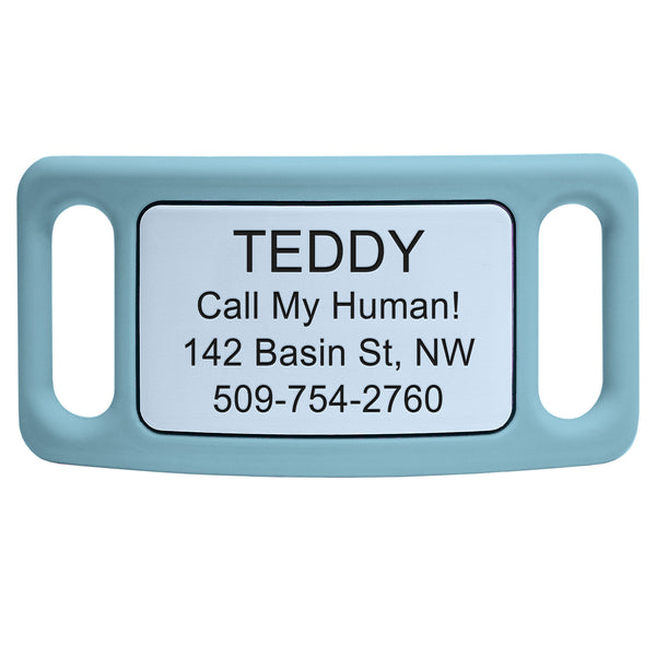 Close-up of light blue Silent Slide-On pet ID tag showcasing engraved example text TEDDY Call My Human 142 Basin St NW 509-754-2760 on white background