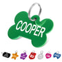 Close-up of green aluminum bone-shaped dog tag engraved with name Cooper and split ring on white background