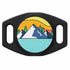 Close-up front of black silicone AirTag holder showing engraved mountain-and-sun design and dual slide-on collar slots on white background