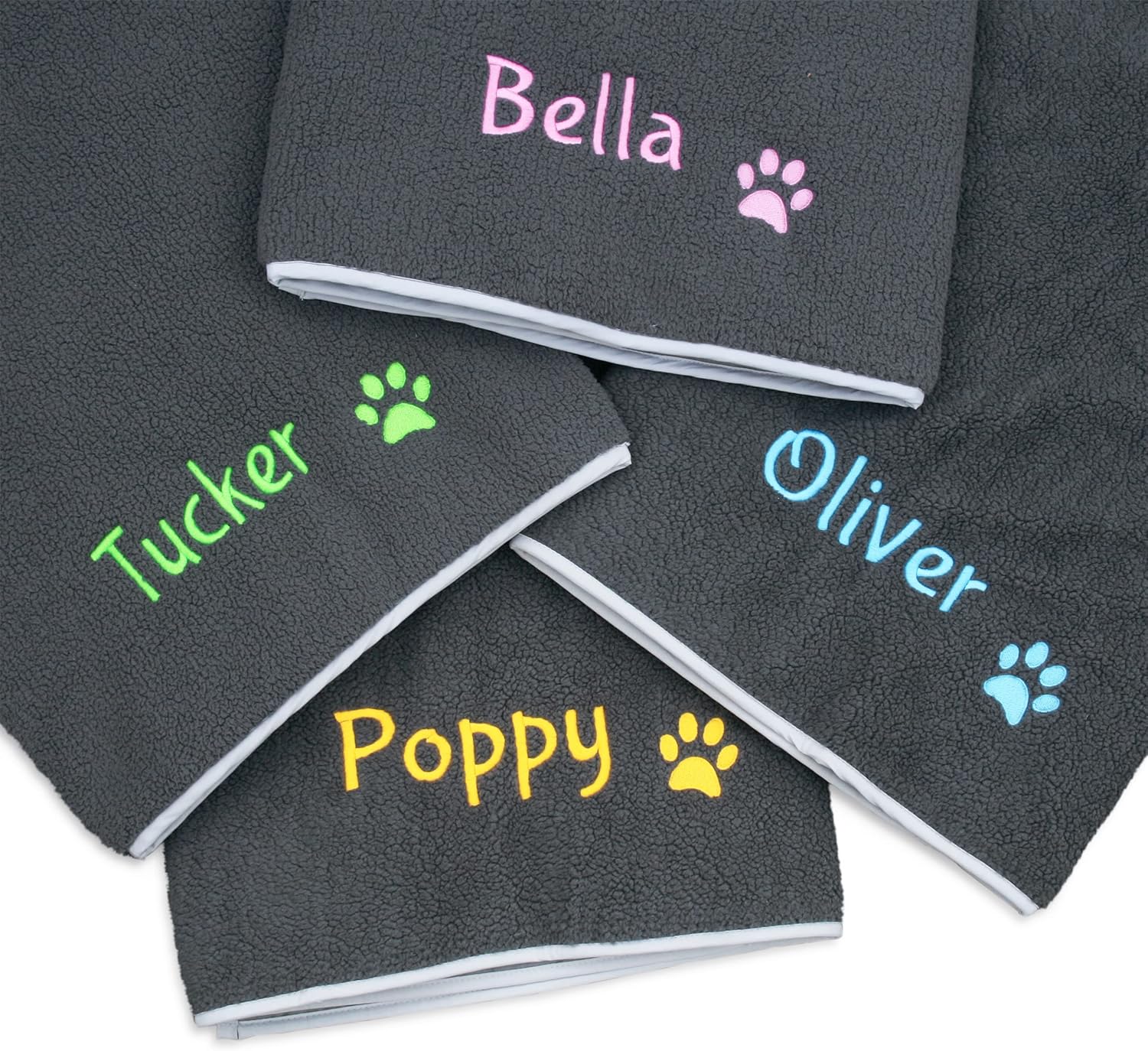 Stacked personalized fleece dog blankets showing embroidered names and paw-print accents in assorted thread colors on gray fleece