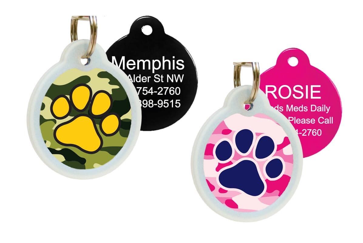 Front view of green and pink camouflage pet ID tags showcasing paw-print design and glow-in-the-dark silencers on white background