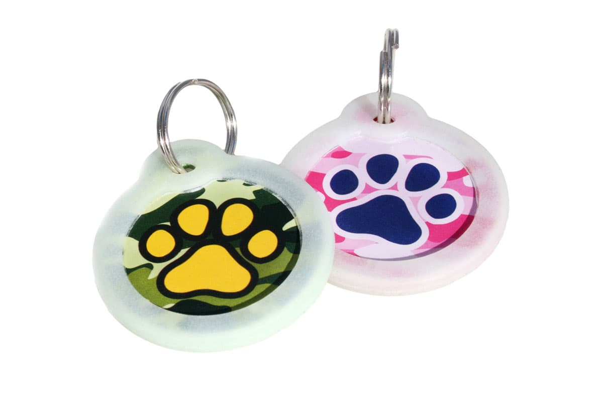 Front view of two camo pet ID tags showing green and pink paw-print design and glow-in-the-dark silencers on white
