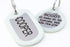 Close-up of stainless steel pet ID tags engraved COOPER and SCOUT with glow-in-the-dark silencers on white background